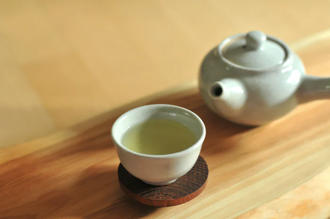Green tea in a white, handle-less cup next to a matching white kyusu teapot.