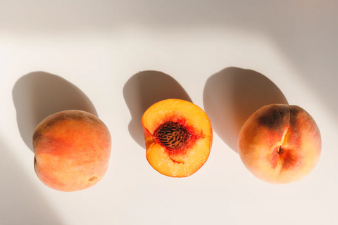 3 yellow peaches on a white background. One peach is cut open to reveal the pit in the middle.