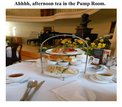 A 3-tiered plate for Afternoon Tea, with sweets at the top, scones in the middle, and sandwiches at the bottom. Two cups of black tea are on the table in white cups.