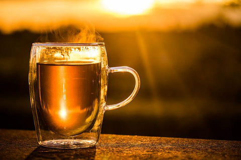 A double-walled glass of black tea against a sunset