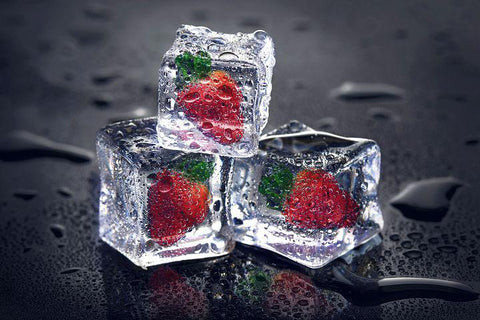3 ice cubes, each containing a frozen strawberry, stacked on a black surface.