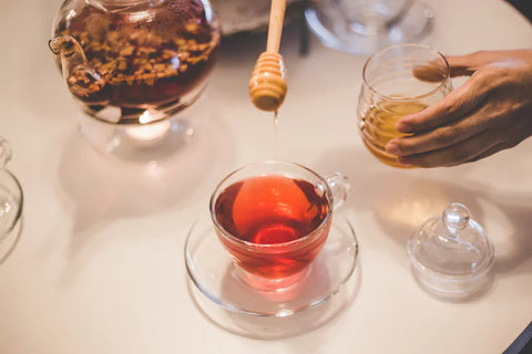 Honey being added to rooibos tea in a glass cup