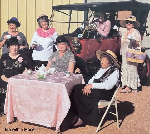 7 women attending a tea service with a restored Model T car in the background