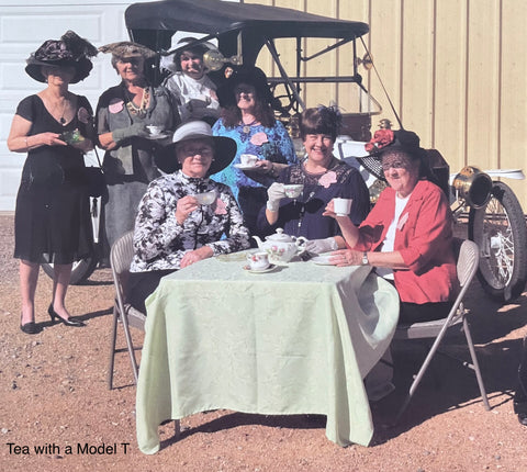 7 women attending a tea service with a restored Model T car in the background