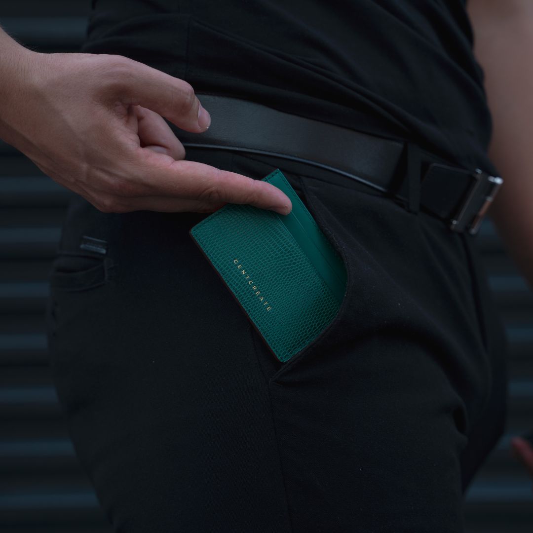 The man inserts a business leather green lizard cardholder into the pocket of his black pants.