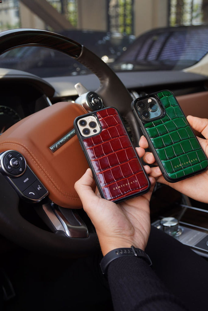 "Un hombre sostiene fundas de cuero para iPhone en estilo cocodrilo brillante, disponibles en colores burdeos y verde.