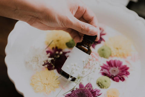 botanical flowers in a bowl with person's hand holding essential oil bottle on top