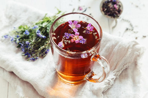 herbal tea in a clear glass with natural flowers in and around it