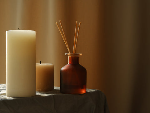 two candles and a diffuser bottle with diffuser sticks inside