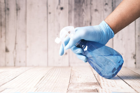 person's hand with gloves holding cleaning bottle