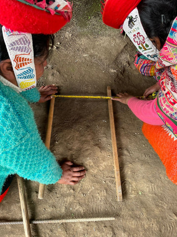 Two indigenous women work together to measure the width of a backstrap loom