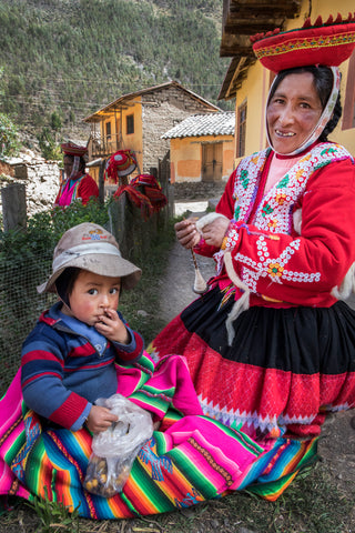 Mother sits down with her child while she spins yarn and he enjoys a snack