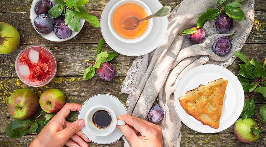 A person holds a cup of coffee and a slice of pie, enjoying a picnic with food served in sustainable soup bowls, plates, and cups.