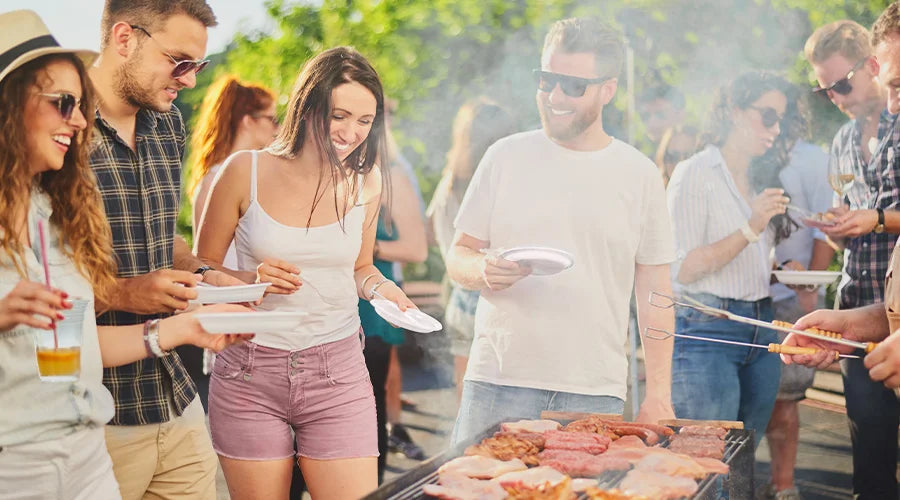 A group of people standing around a barbecue, enjoying an eco-friendly picnic with compostable plates and cutlery.