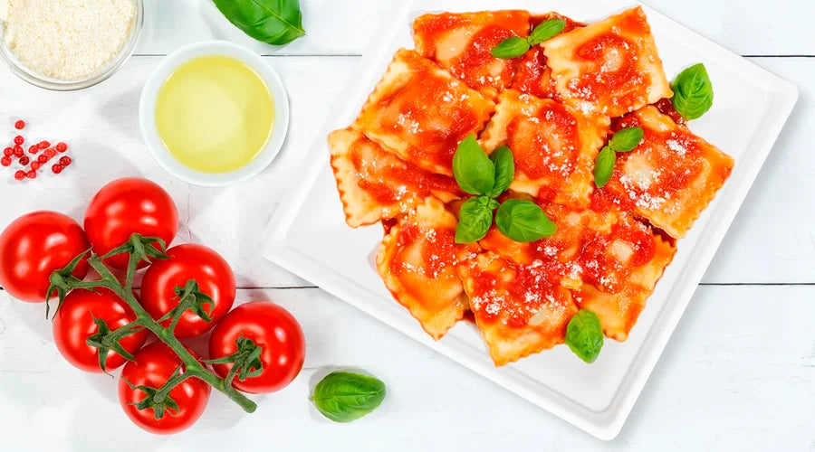 A plate of ravioli topped with tomatoes and basil, served on Sugarcane Bagasse Plates.