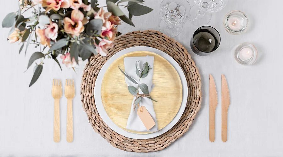 A place setting with a white napkin and a wooden knife on compostable plates and alongside compostable forks.