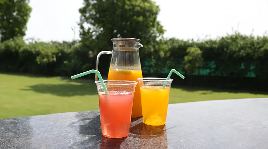 Two glasses of orange juice and a pitcher with compostable straws