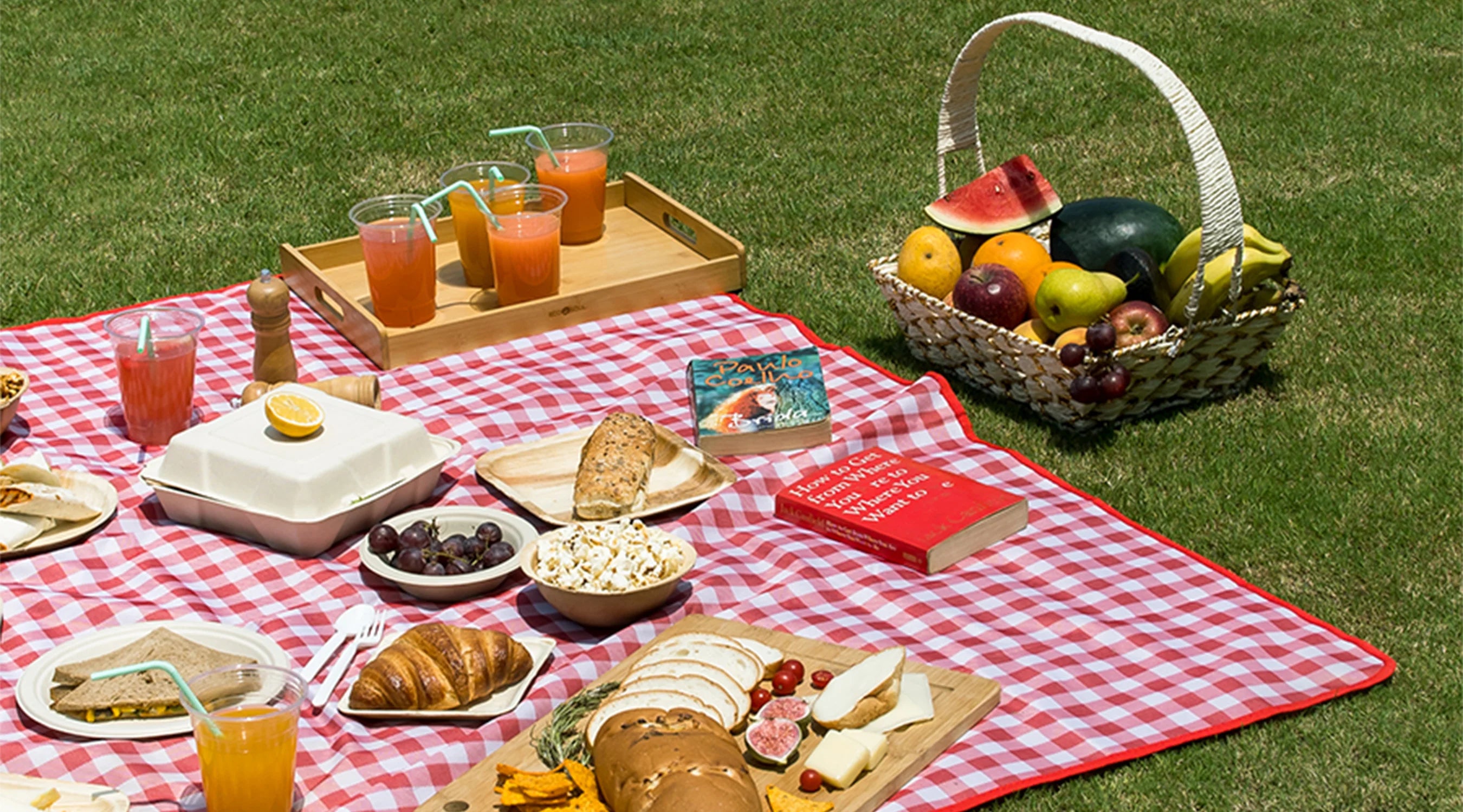 A picnic table set with fresh fruit, bread, and drinks, showcasing eco-friendly picnic products.