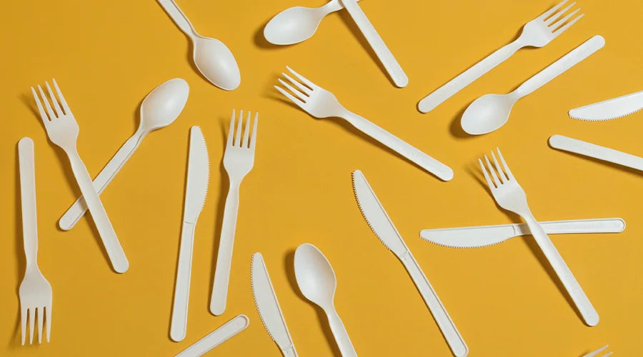 White compostable forks and spoons neatly arranged on a vibrant yellow background.