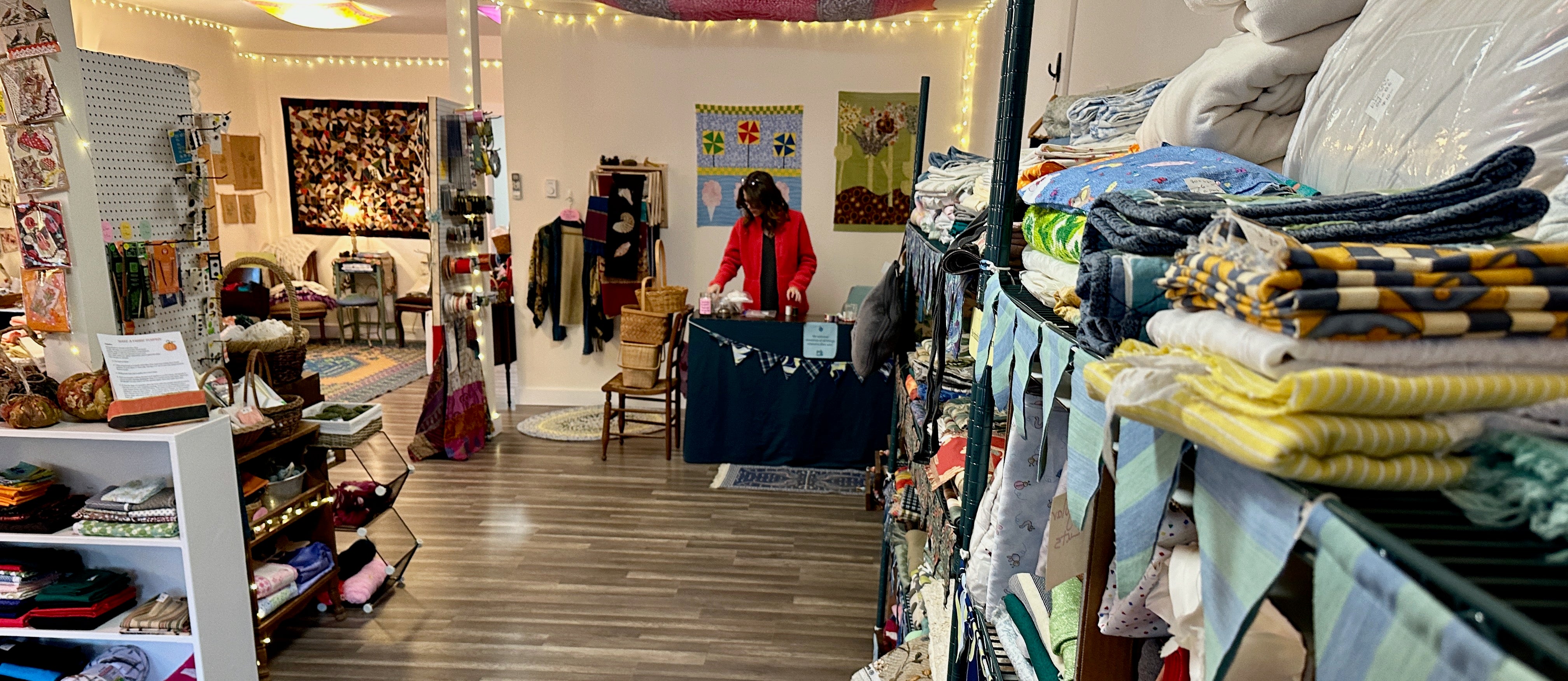 A woman in a red sweater is at a desk in a shop with fabric and notions