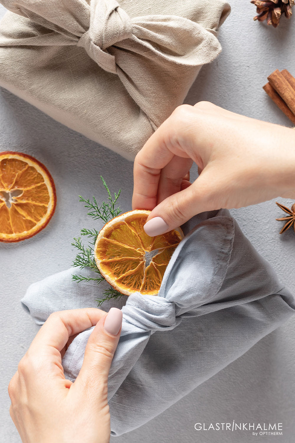 Furoshiki und die simple und effektive Falttechnik: Verpackte Geschenke mit hellgrauem und beigen Tuch und werden mit getrockneten Orangenscheiben dekoriert