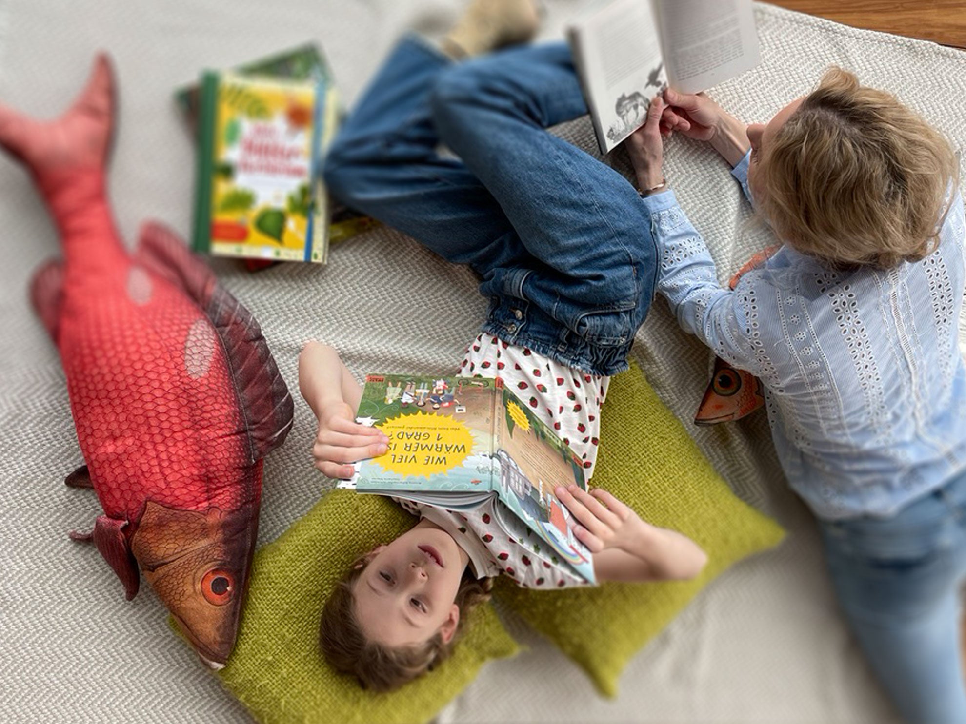 Mutter und Tochter liegen gemütlich auf dem Boden mit Decke und Kissen und lesen Bücher