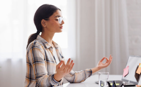 Young woman with glasses practicing meditation at her desk, using mindfulness to manage stress during work at home