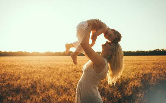 Happy mother lifting toddler in sunlit field, joyful mother-child bonding moment, playful parenting outdoors, loving mom and child in nature, golden hour family time, maternal affection and care in summer field