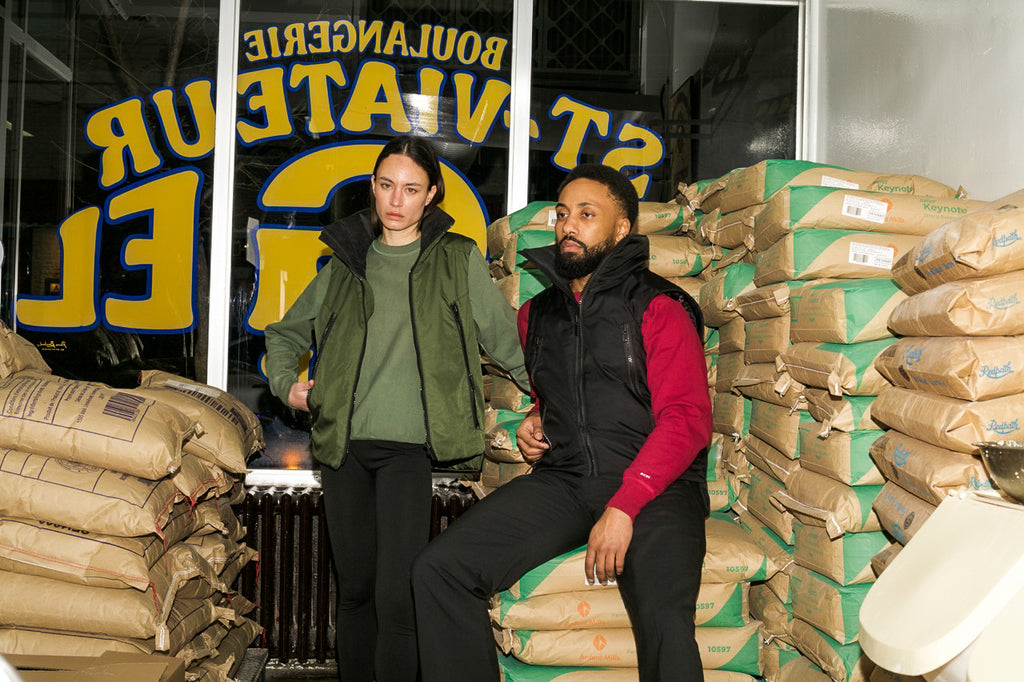 Female and male model wearing the MYLES crewnecks underneath the new MONTCALM vest at bagel ST-Viateur, staple of the MILE-END