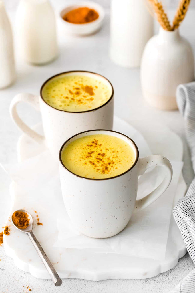 two white mugs filled with turmeric latte displayed on a white table