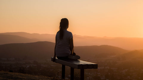 a woman sitting on top of a mountain staring at the horizon at dawn