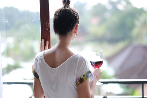 Woman holding glass of red wine looking out the window