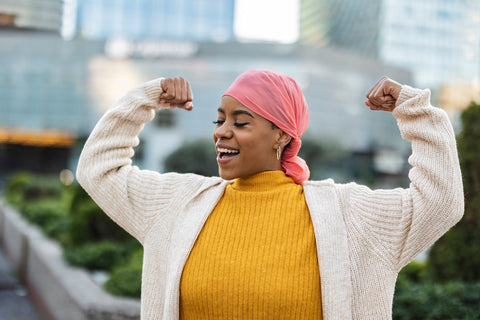 Woman fighting breast cancer wears a pink scarf and clenches her arms as a survivor fighter