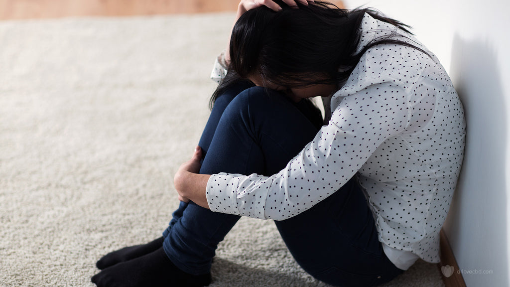 photo of a young woman with anxiety sitting on the carpet back to the wall with head down