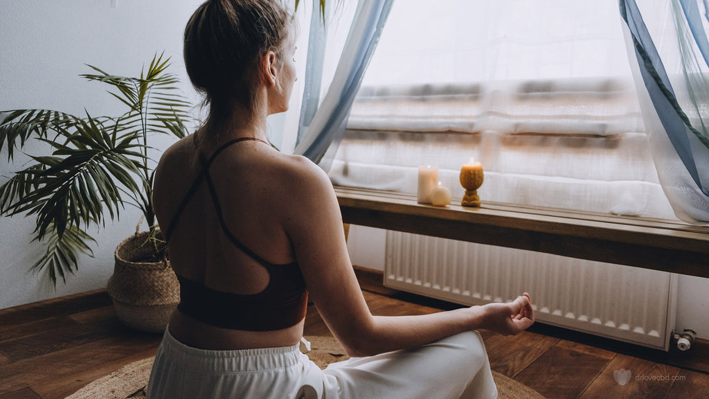 young woman at peace meditating at home beside the window with plants and candles