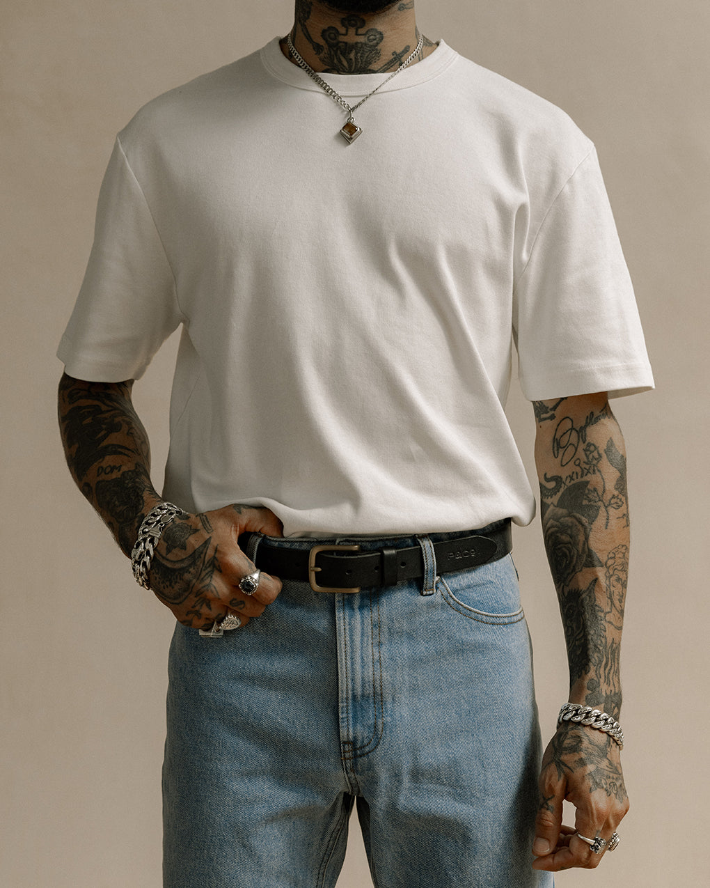 Man with a sleeve of tattoos wearing P and Co heavyweight white crewneck tee with medium blue jeans and black leather belt