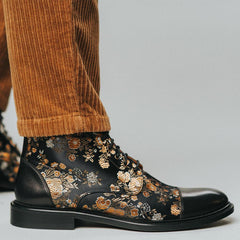 Masculine-presenting person wearing corduroy pants and black, leather boots with a floral pattern