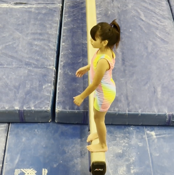 girl wears a rainbow pattern gymnastics biketard practice on the beam