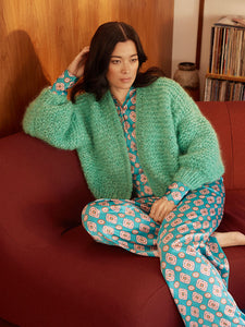 Woman lounges on maroon couch wearing a teal colours fluffy knitted mohair jumper and a satin shirt and pants. 