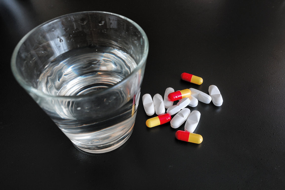 Glass of water next to Benadryl and melatonin pills on a dark surface