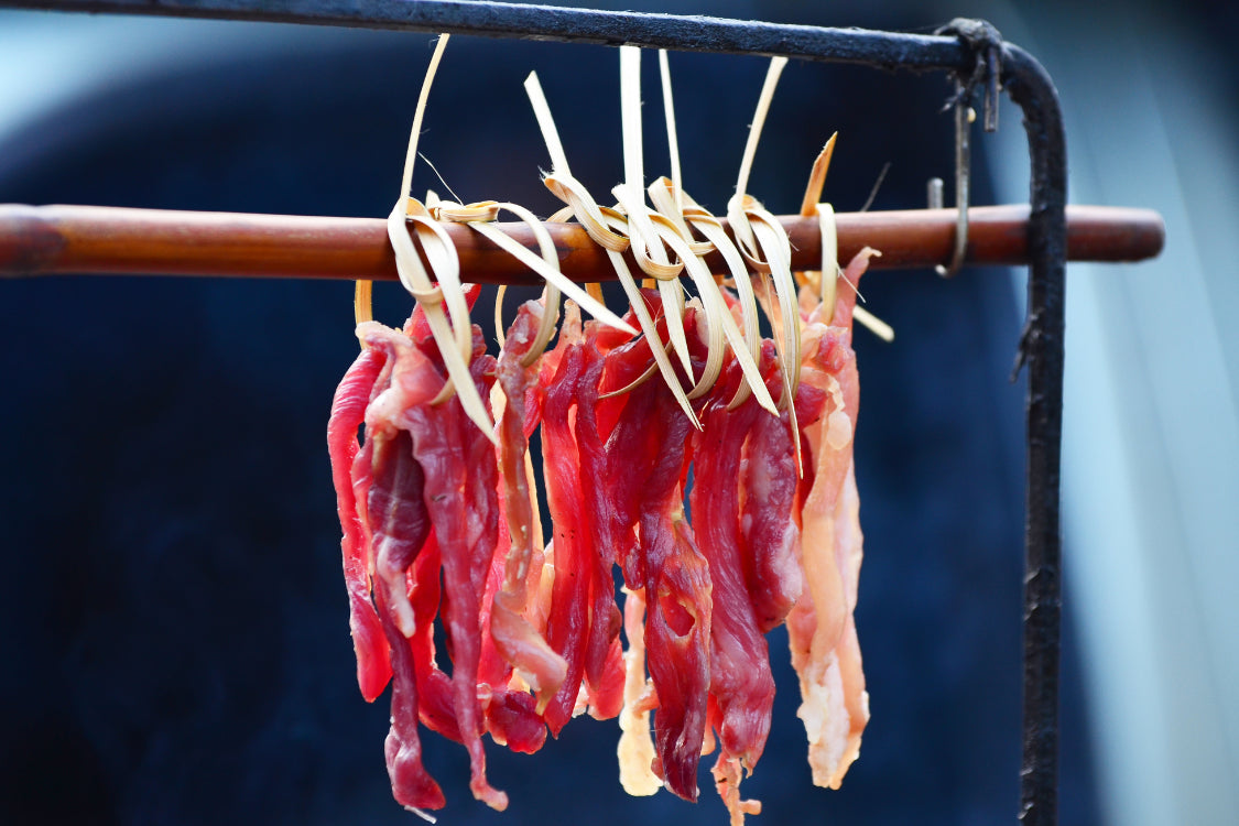 Raw beef strips hanging on a bamboo rack for traditional air drying