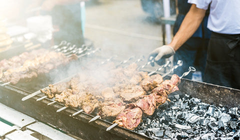 Ein traditioneller Mangal-Grill, auf dem frische Schaschlikspieße mit mariniertem Fleisch zubereitet werden. Die Glut glüht und das Aroma des Grills vermischt sich mit dem Duft des Fleisches, das auf den Spießen gegrillt wird