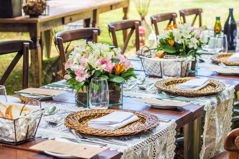 An outdoor table setting dressed with table cloths, plates, flowers and glasses