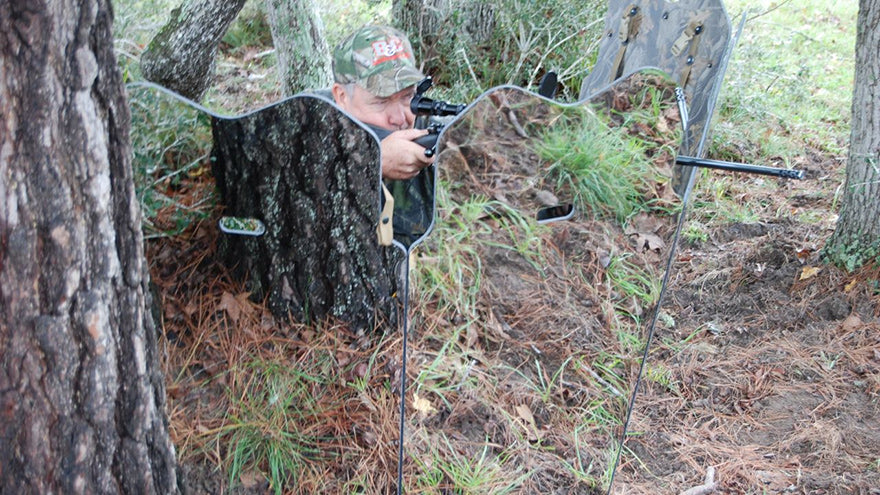 a hunter with a rifle using a mirrored ground blind