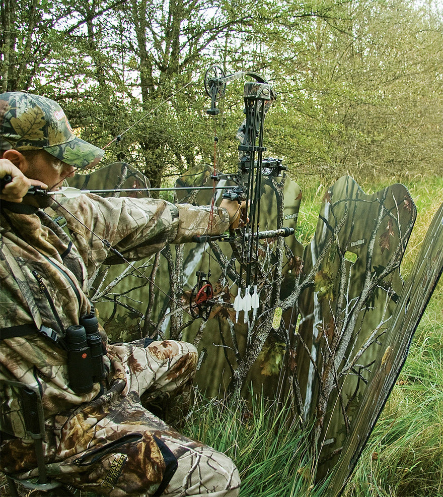 a hunter using a compound bow behind a blind