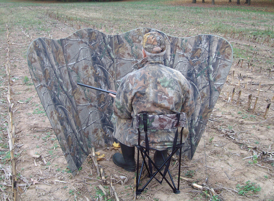 man sitting behind blind holding rifle