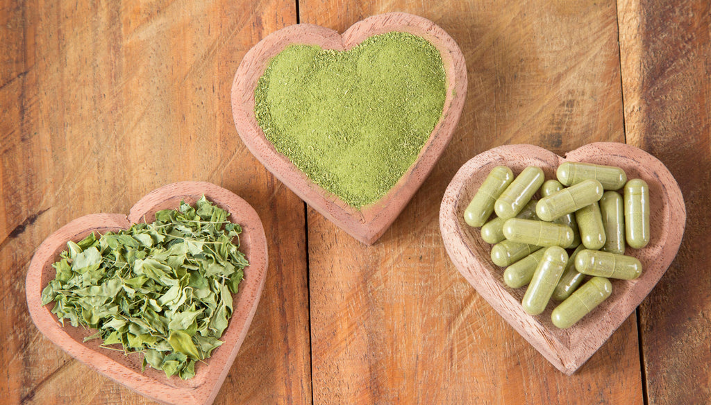 Moringa in powder, capsule and leaves on heart cups on a wooden table