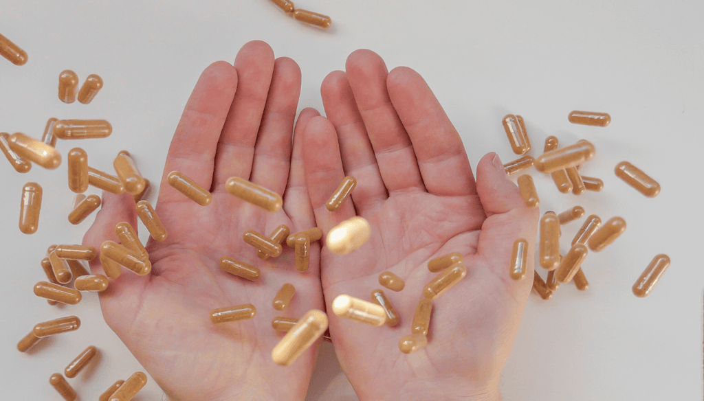 Turmeric capsules falling down on the table and on two hands.