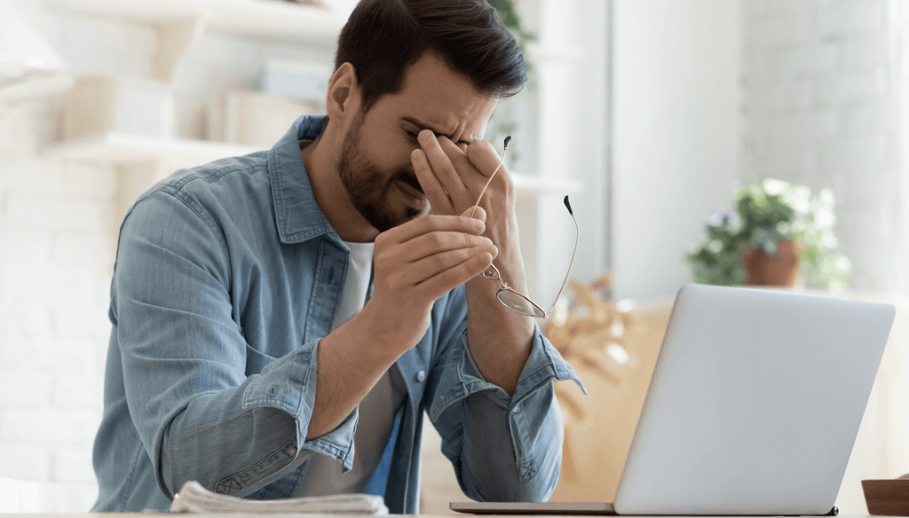 A stressed man working at his computer with headache