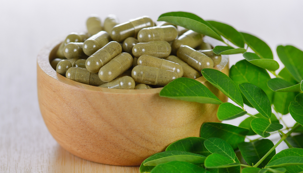 Moringa capsules on a wooden bowl and Moringa leaves